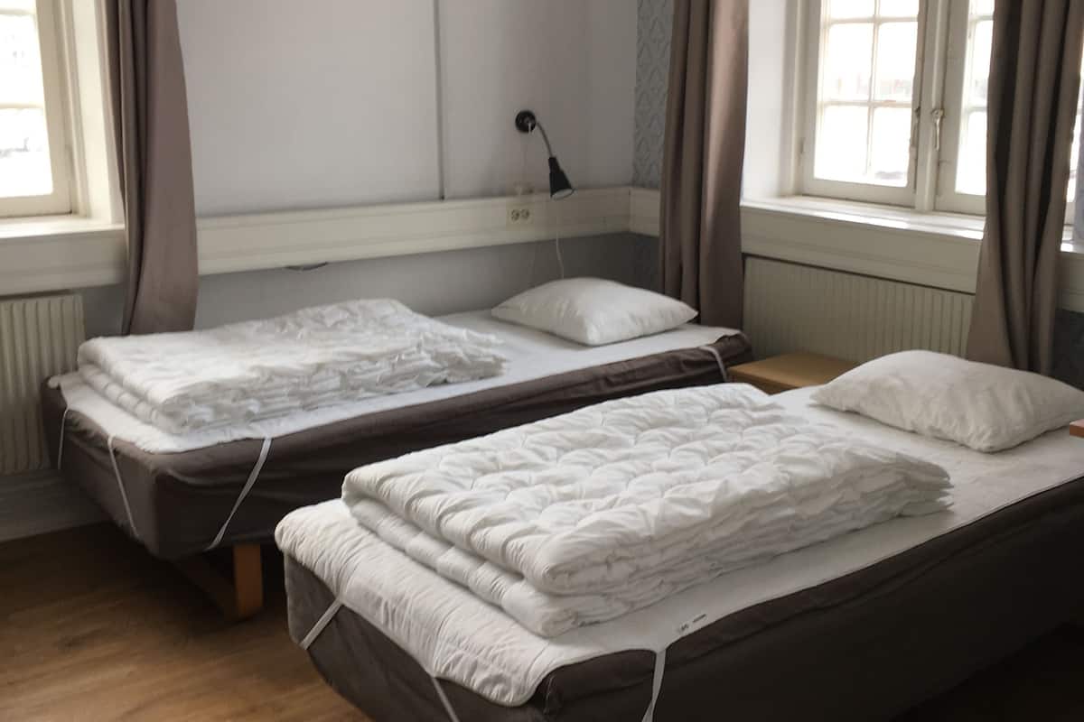A room with two single beds, a flat-screen TV mounted on the wall, and a window with curtains.