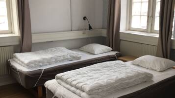 Quarto com duas camas de solteiro, uma televisão de tela plana na parede e uma janela com cortinas.