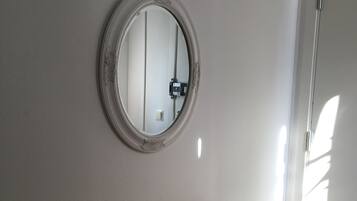 Een kamer met een houten tafel, een stoel, een ronde spiegel aan de muur en een deur.