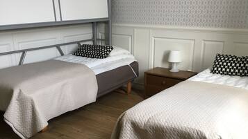 Een hotelkamer met twee eenpersoonsbedden, houten vloeren, een witte garderobe en behang met een patroon.
