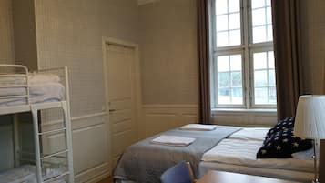 Hotelkamer met een stapelbed, een enkel bed, een bureau met lamp en een raam met gordijnen.