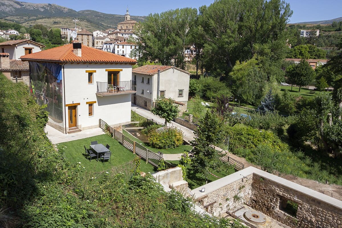 A two-story house with a balcony, a small garden, and a stone wall.