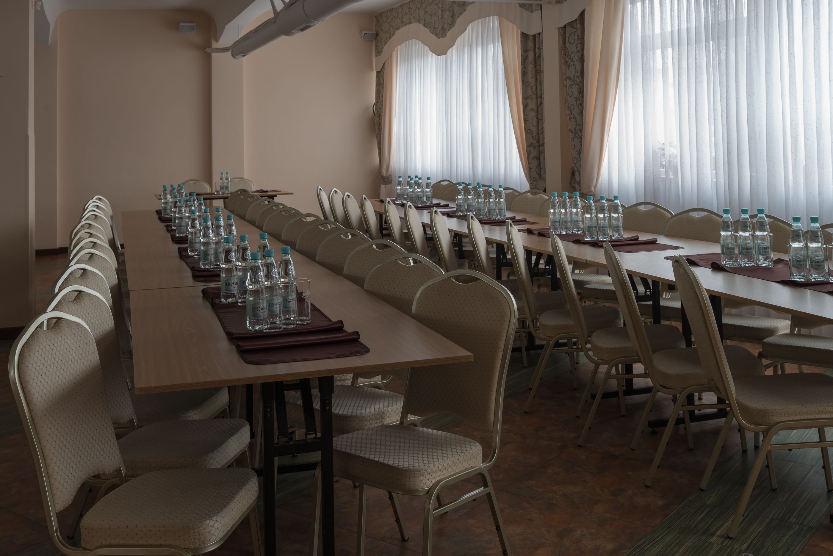 A conference room with long tables and chairs, water bottles, and a large window with curtains.
