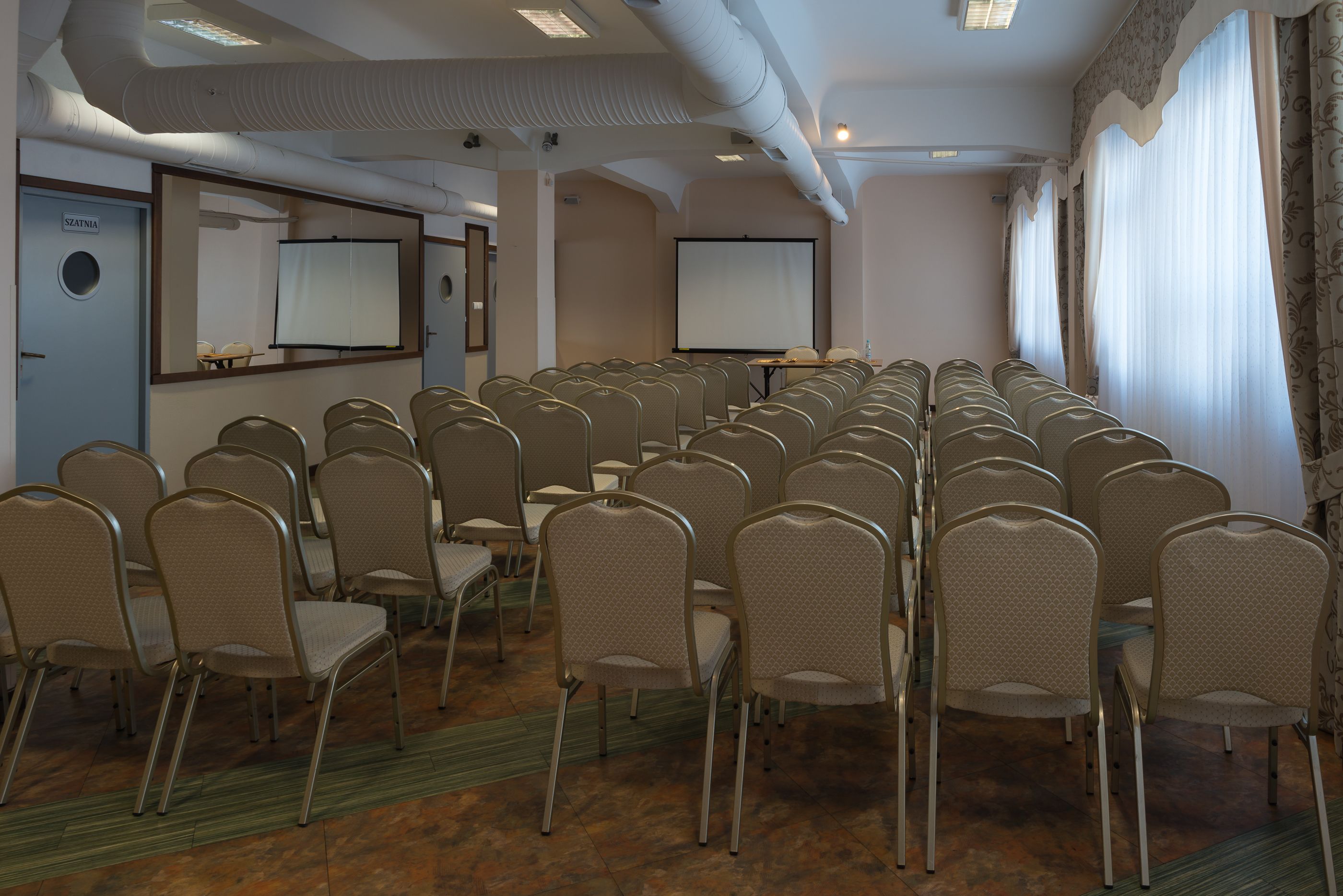 A conference room with rows of chairs, a projector screen, and a whiteboard.