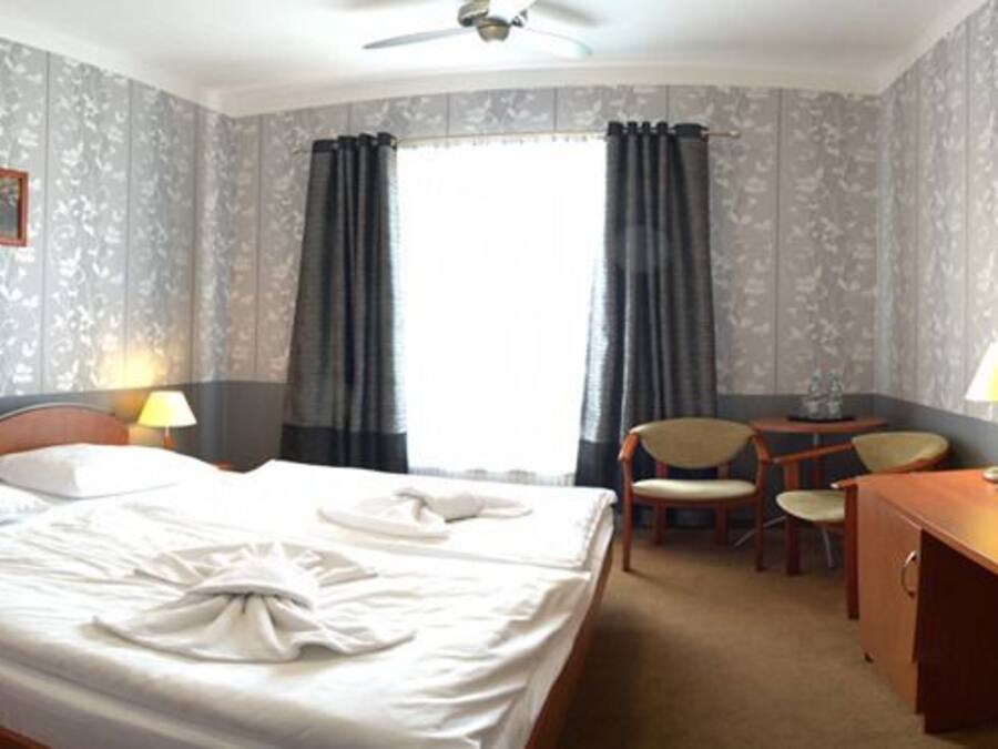 Habitación de hotel con cama, mesitas de noche, escritorio, silla, televisor y ventana con cortinas.