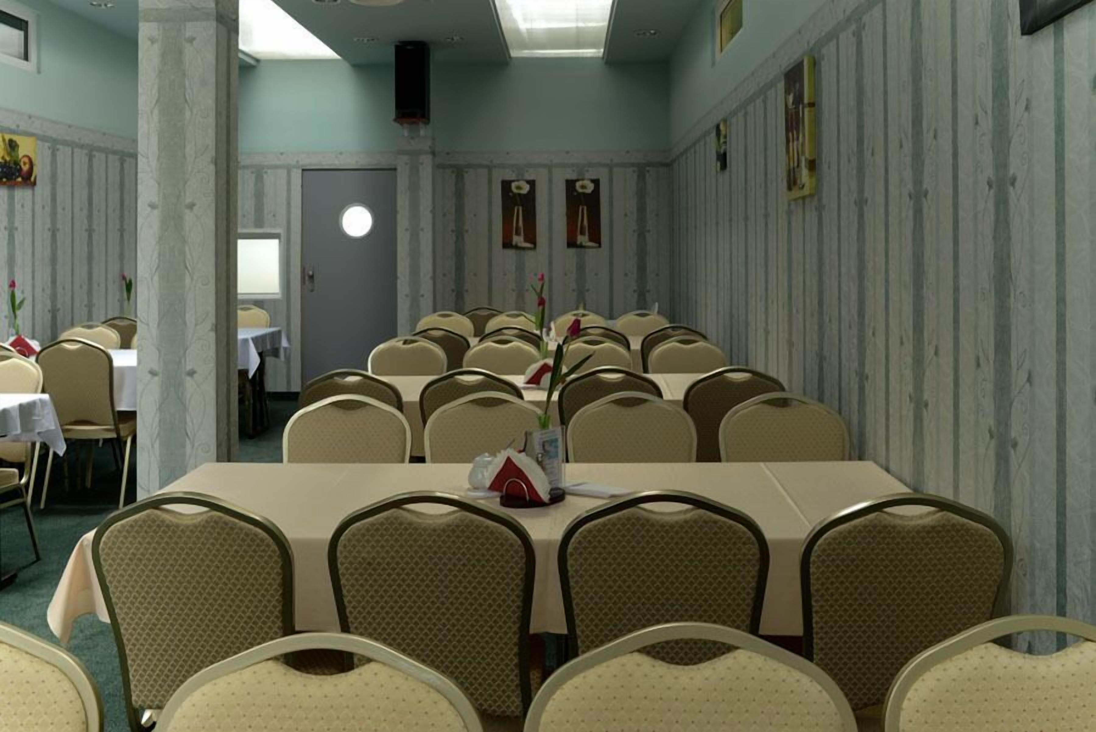 A conference room with multiple tables and chairs, a speaker, and framed pictures on the walls.
