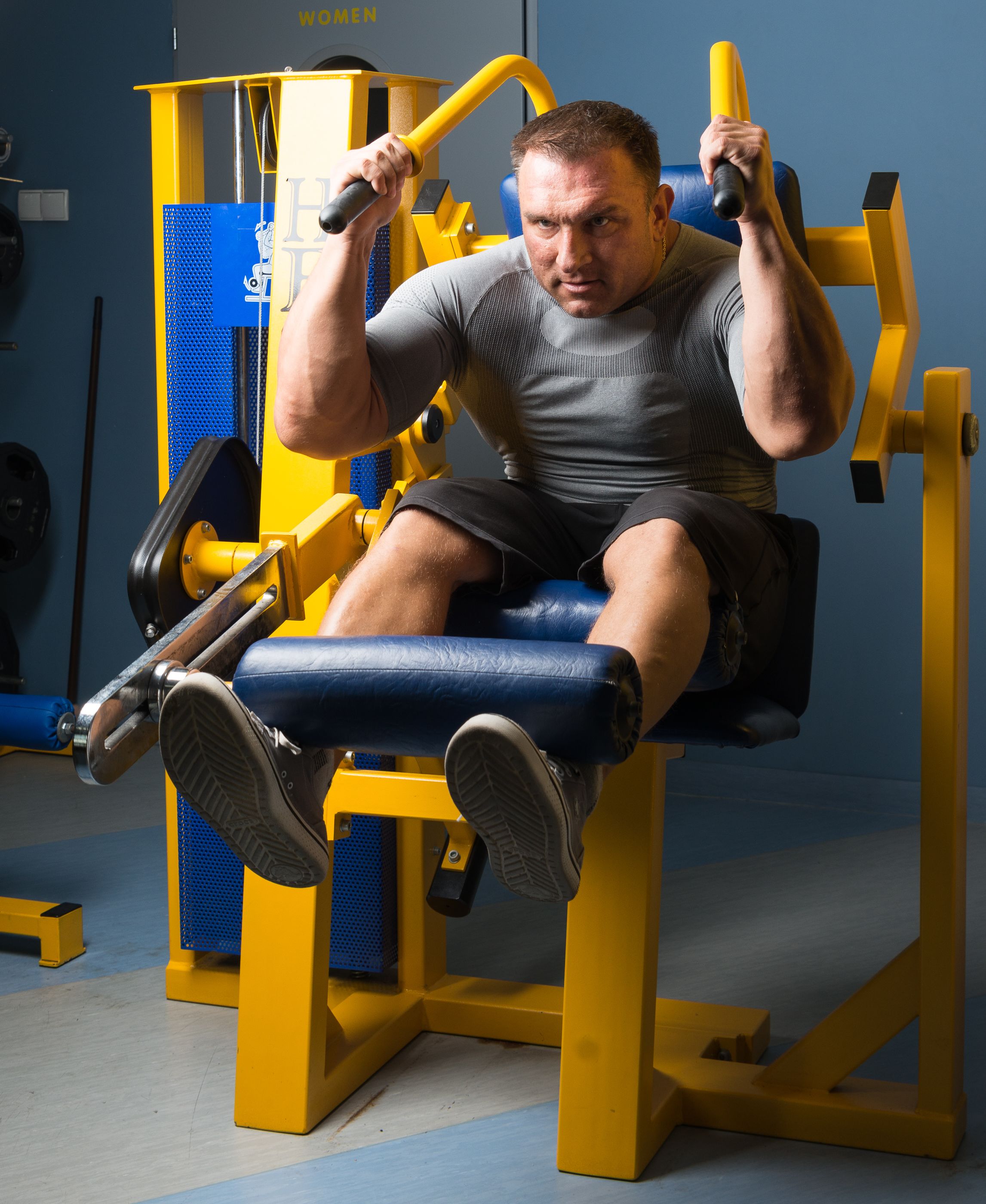 Een man gebruikt een gele en blauwe trainingsmachine in een sportschool.