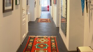 A hallway with a patterned rug, framed artwork on the walls, and a coat rack with hangers. - Soho Apartments - Grand Soho (Vienna)