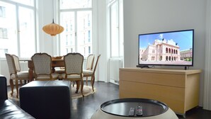 A living room with a television, a dining table with chairs, a sofa, and a coffee table. - Soho Apartments - Grand Soho (Vienna)