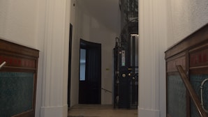 A staircase leading to a dark room with a door, white walls, and a chandelier. - Soho Apartments - Grand Soho (Vienna)