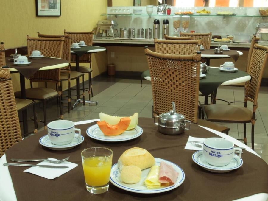A breakfast setting with wicker chairs, a buffet area in the background, and a table with plates of food, a jug of orange juice, and a teapot.