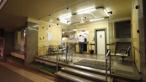 Un hall de hotel con mostrador de recepción, un área de espera con sillas y una escalera que conduce a un piso superior.