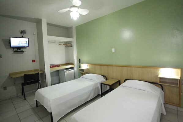A hotel room with two single beds, a desk with a chair, a small table, a TV, and a ceiling fan.