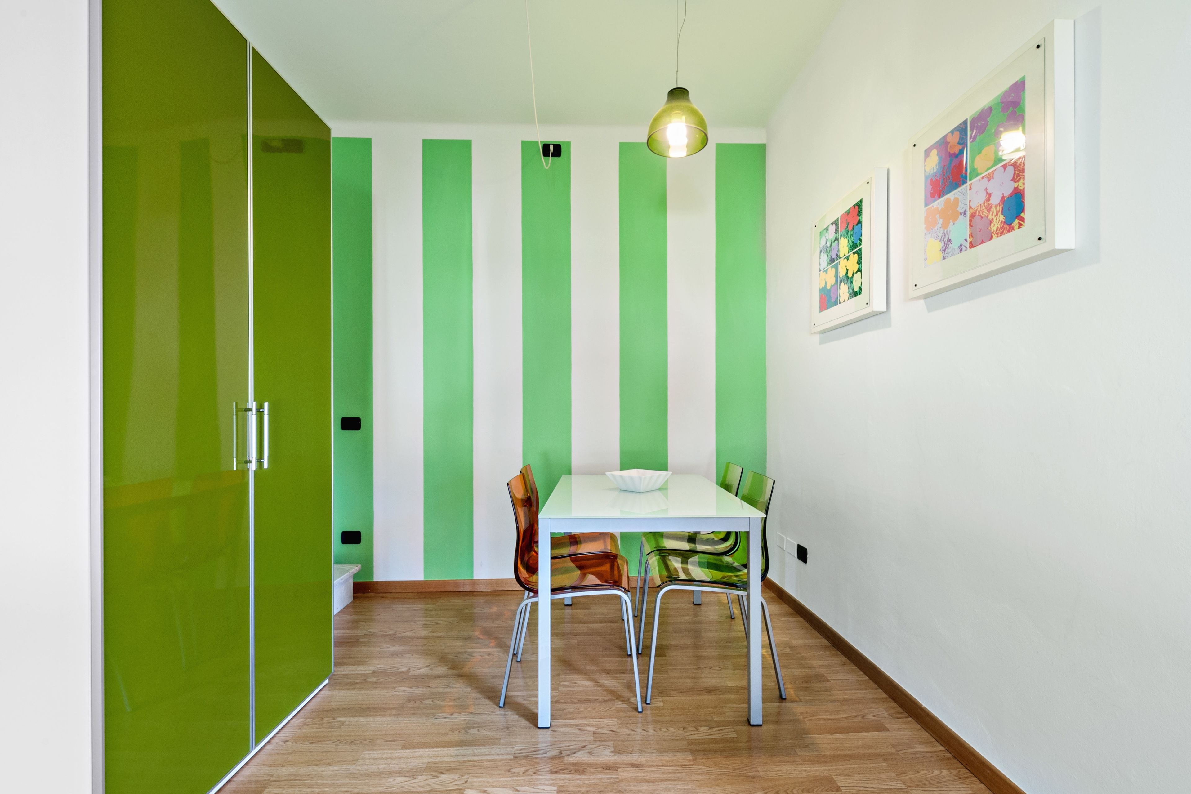 A dining area with a white table and chairs, green striped walls, and a hanging light fixture.