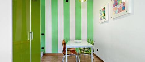 A dining area with a white table and chairs, green striped walls, and a hanging light fixture.