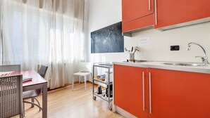 A compact kitchen with orange cabinets, a white countertop, and a small dining area with a table and chairs. - Lucca in Villa San Marco (Lucca)