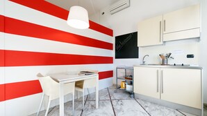 A modern kitchen with a white and red striped wall, a white table with a chair, and a small island with a sink and utensils. - Lucca in Villa San Marco (Lucca)
