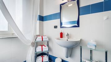 Un baño con lavamanos blanco, azulejos azules, un estante de vidrio con artículos de aseo personal y un perchero con toallas dobladas con cuidado.