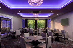A restaurant with multiple tables and chairs, a chandelier, and large windows with a view of greenery. - Dalmeny Park House Hotel (Glasgow)