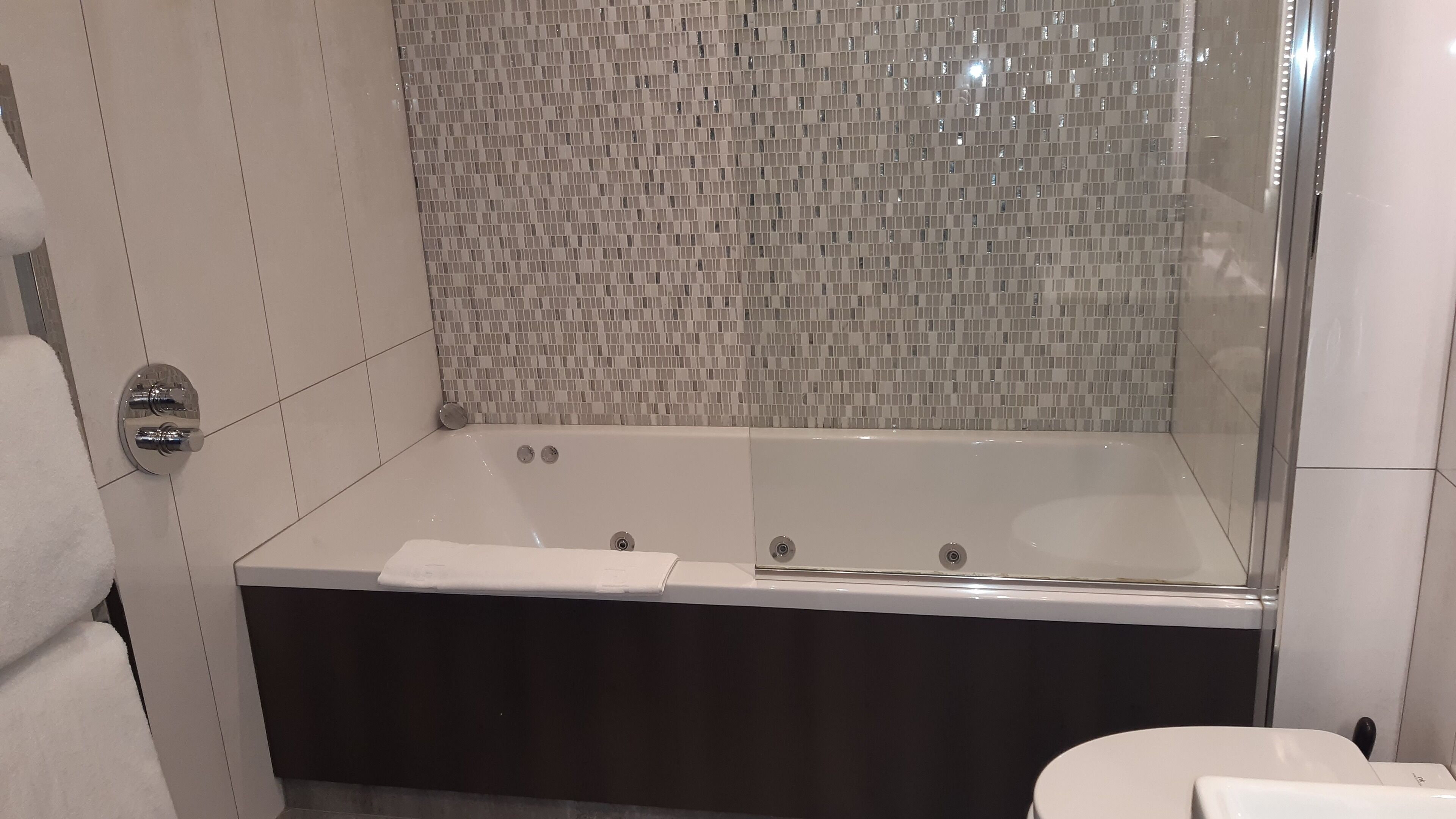 Un baño moderno con bañera acristalada, azulejos blancos y una zona de ducha visible.