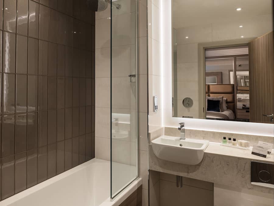A modern bathroom with a glass-enclosed shower, a white sink, and a vanity with toiletries.