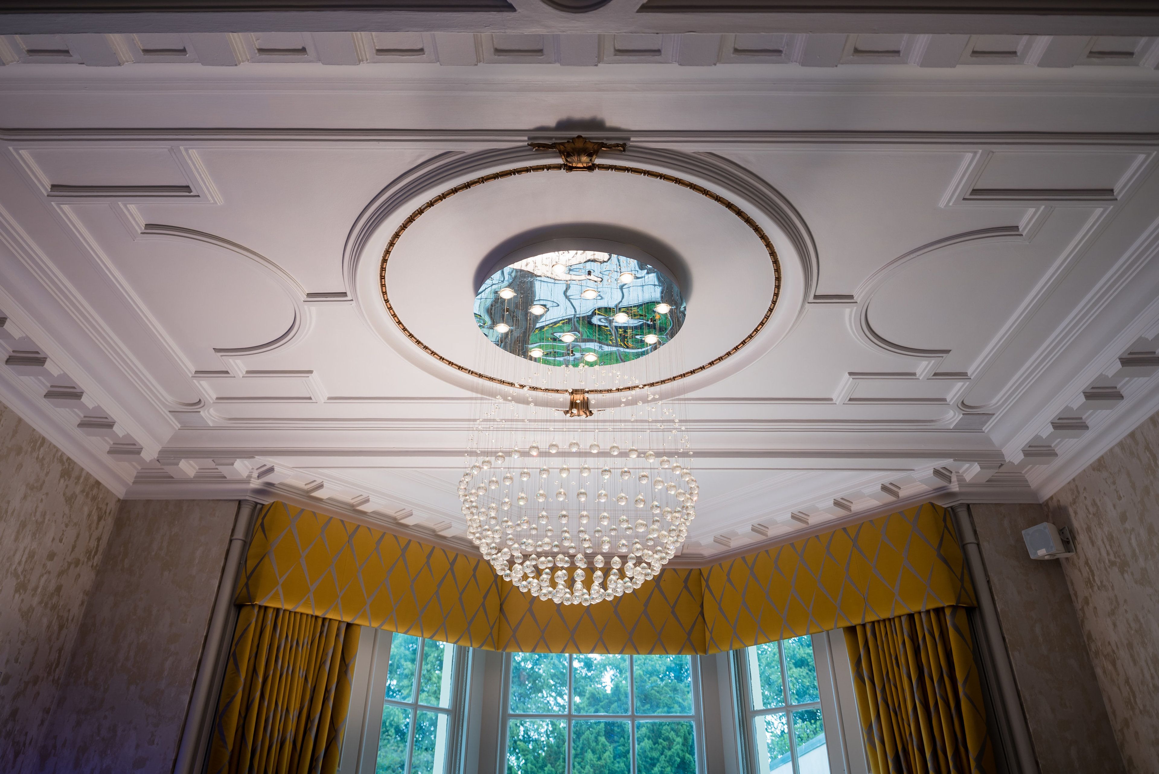 A room with a large circular stained glass window, a chandelier, and yellow curtains.
