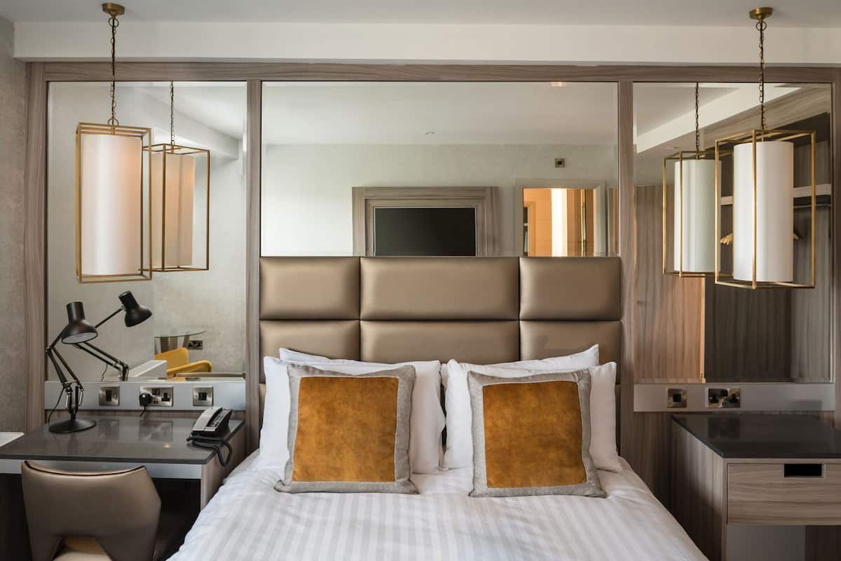 A hotel room with a bed, bedside table, desk, and a large mirror.