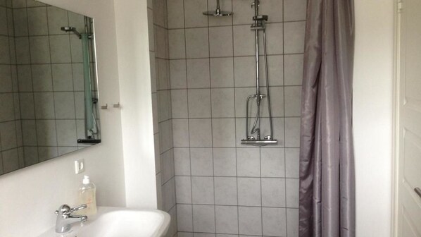Un baño con lavamanos blanco, un espejo, una ducha con cabezal de ducha de mano y una cortina.