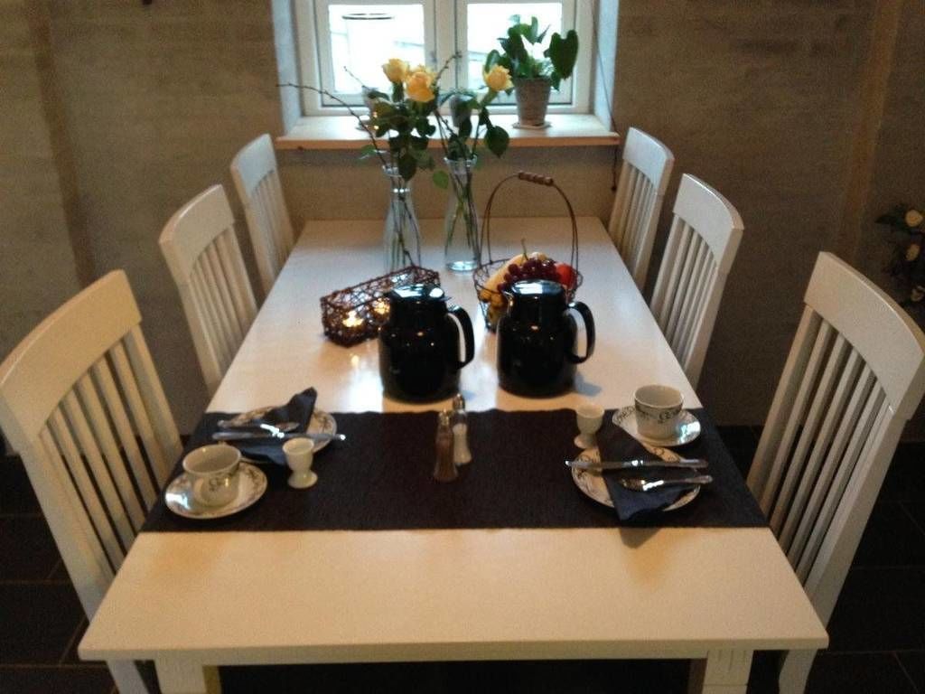 Una mesa de comedor dispuesta con una cafetera, tazas y una cesta de fruta.