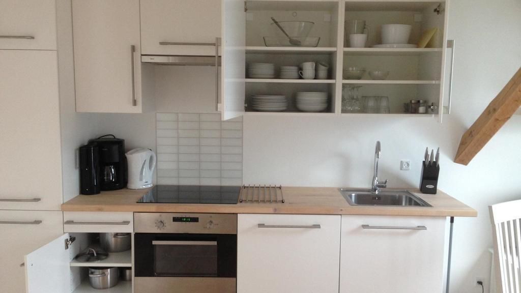 Una cocina compacta con armarios blancos, horno integrado, cafetera y escurreplatos.