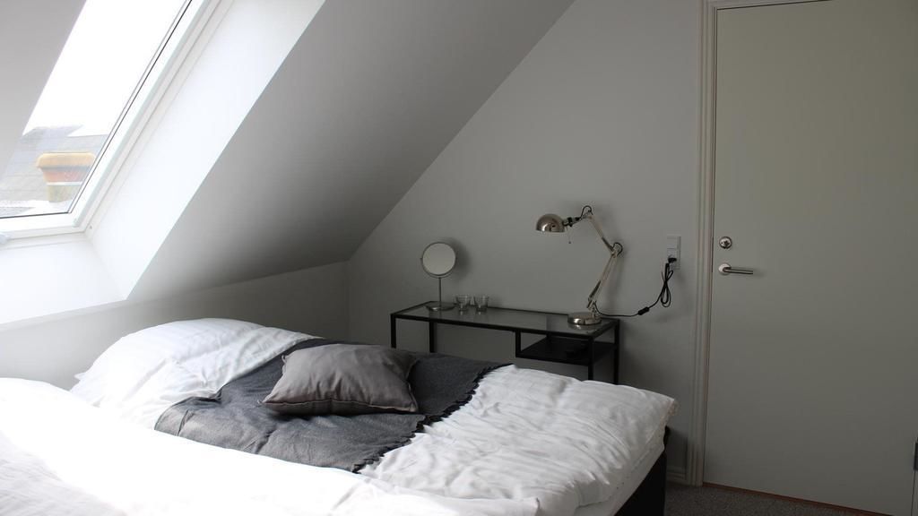 A bedroom with a sloped ceiling, a bed with white and gray bedding, a bedside table with a lamp, and a door with a handle.