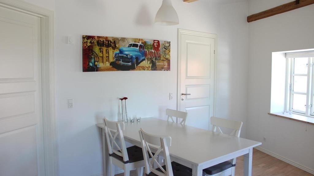 A dining area with a white table and chairs, a painting on the wall, and a window with natural light.