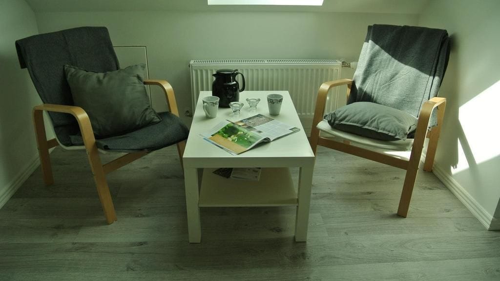 Una habitación pequeña con dos sillas de madera, una mesa blanca y una ventana.