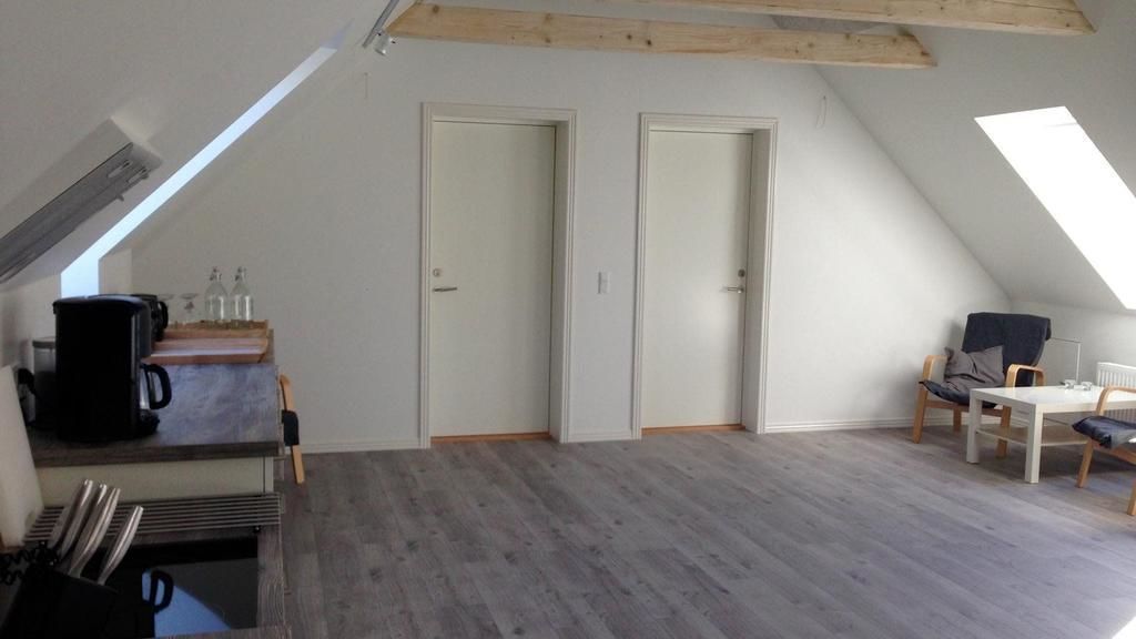 Ein Loftzimmer mit schrägem Dach, Holzbalken, einer Küchenzeile, einer Essecke mit Tisch und Stühlen sowie zwei Türen.