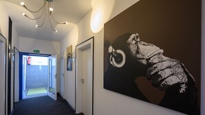 En hall med en stor svartvit väggmålning som föreställer en hand som håller i ett kugghjul, en brandsläckare och en dörr som leder till ett badrum.