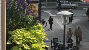En gatubild med en skylt som visar namnet ”Heymann”, uteservering och en gångbana för fotgängare.