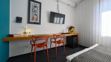 A hotel room with a bed, a desk with a computer, two orange chairs, a television, and a Buddha statue.