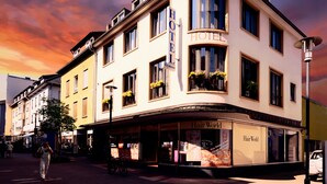 Ett hotell med en butik som säljer hårprodukter på bottenvåningen, många fönster och en balkong med blommor.