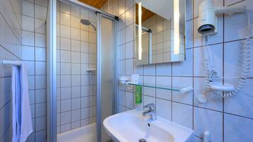 A bathroom with a glass shower enclosure, a sink, a mirror, and a hairdryer mounted on the wall.
