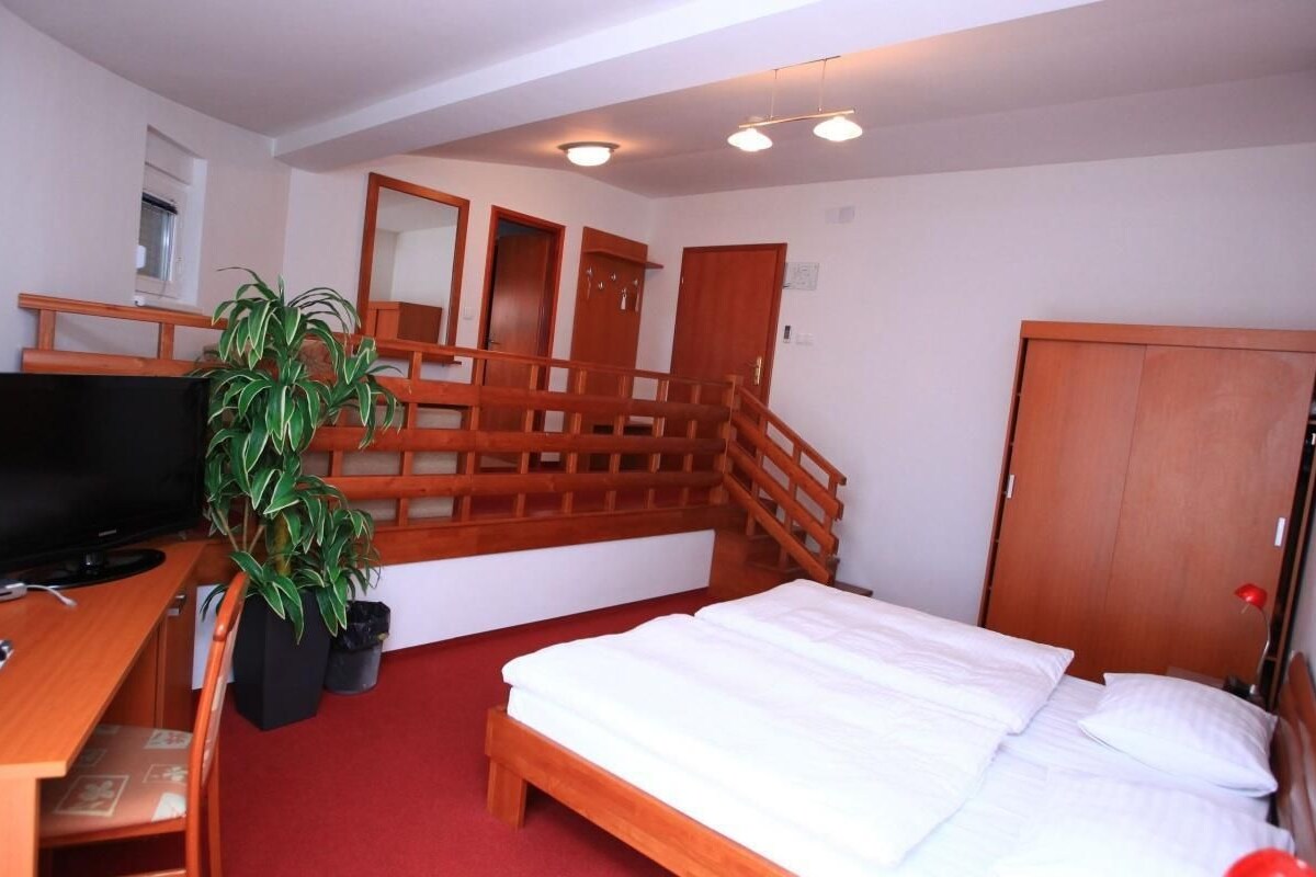 A hotel room with a bed, a desk with a television, a plant, and a staircase.
