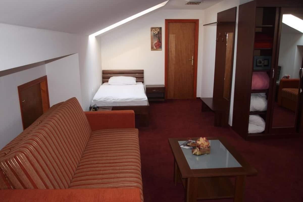 A hotel room with a bed, a sofa, a table, and a wardrobe.