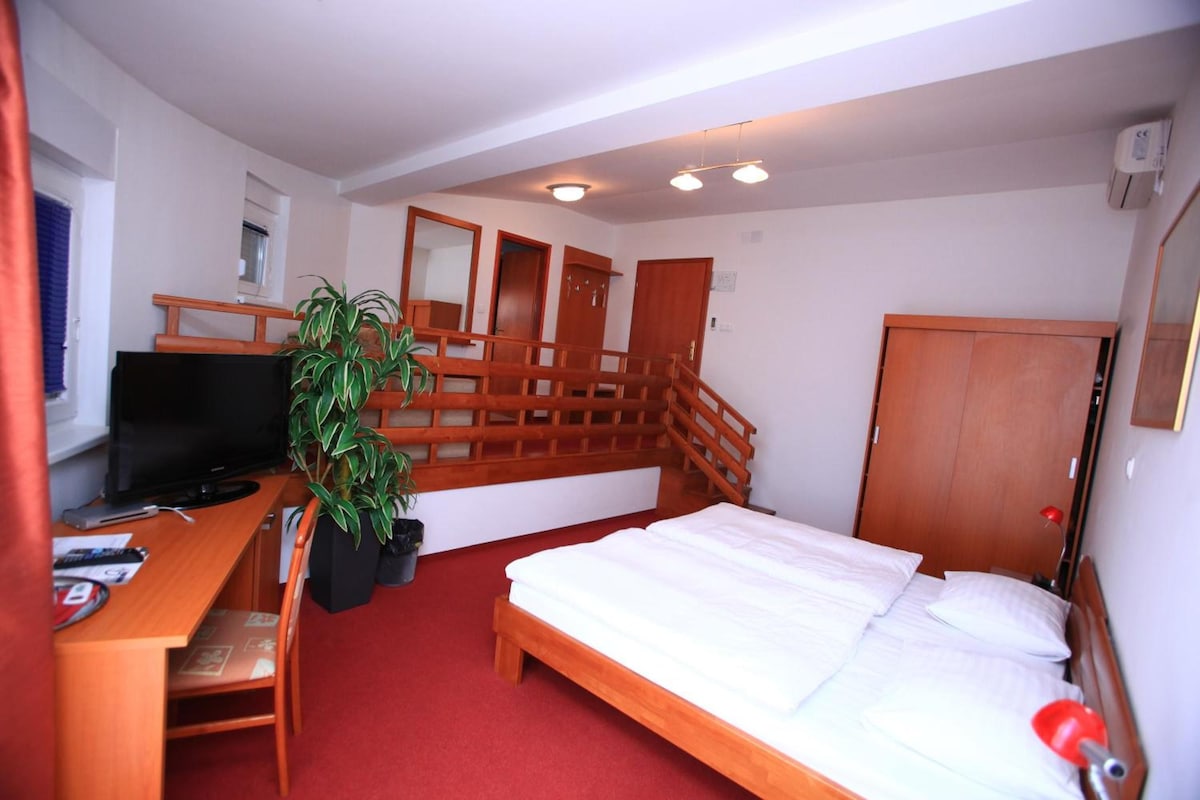 A hotel room with a bed, a desk with a television, a plant, and a staircase.