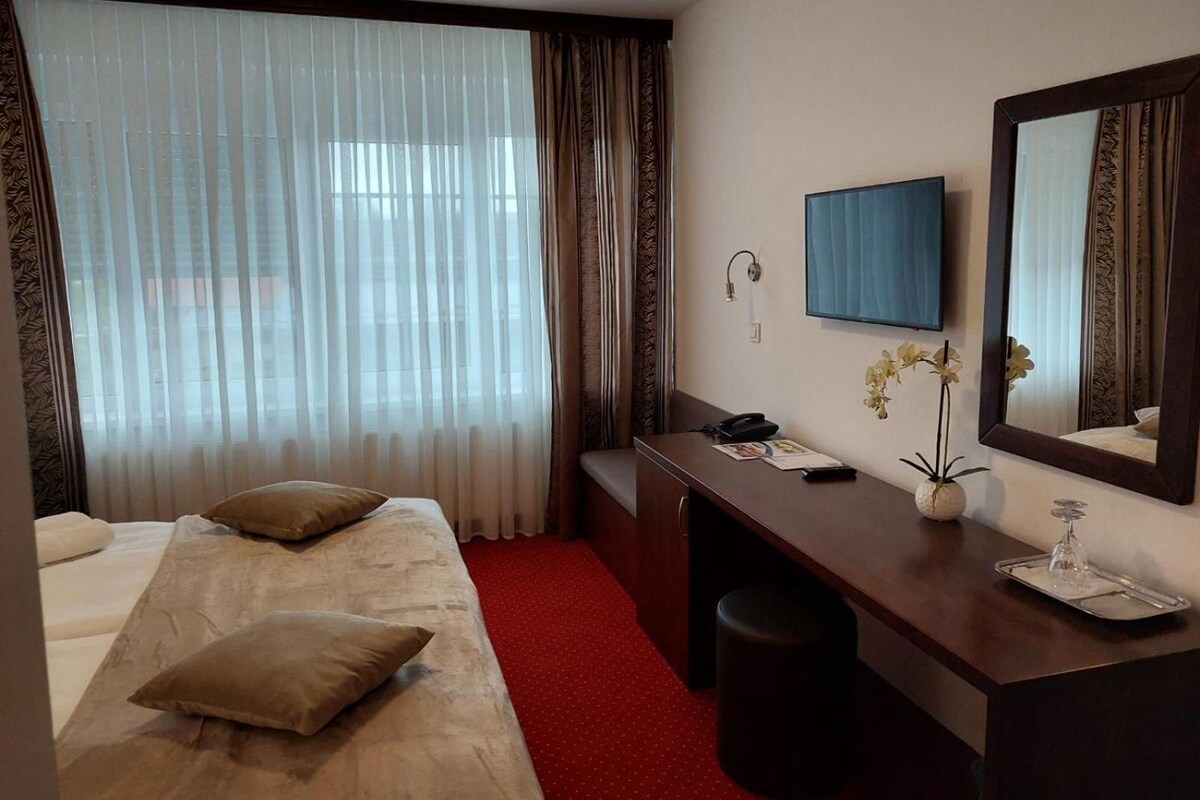 Ein Hotelzimmer mit einem Bett, einem Schreibtisch, einem Stuhl, einem Fernseher und einem Fenster mit Vorhängen.