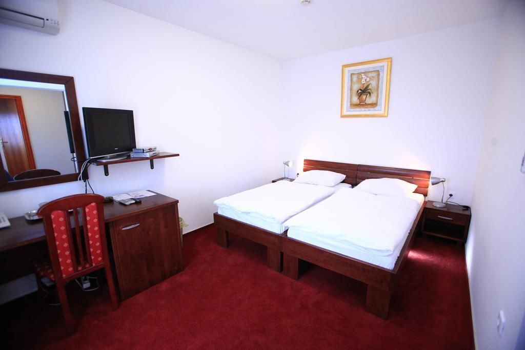 Habitación de hotel con dos camas, un escritorio, una silla, un televisor y un cuadro en la pared.