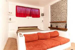 Une chambre à coucher avec un lit, un rideau rouge, un mur orné d’un motif de petits cailloux et une étagère avec des bouteilles.