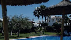 A swimming pool area with white lounge chairs and thatched umbrellas. - Hostal Al-Andalus (La Guijarrosa)