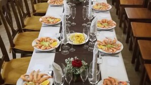 A long dining table set with plates of seafood, wine glasses, and floral centerpieces in a room with wooden chairs and a decorative wall. - Hostal Al-Andalus (La Guijarrosa)