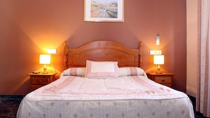A neatly made bed with a wooden headboard, two bedside tables with lamps, and a framed picture on the wall. - Hostal Al-Andalus (La Guijarrosa)