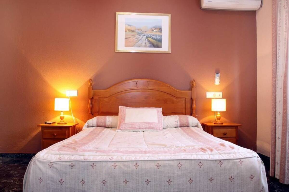 A neatly made bed with a wooden headboard, two bedside tables with lamps, and a framed picture on the wall.