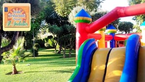 A colorful inflatable play structure with slides and climbing elements, surrounded by a well-maintained garden with trees and grass. - Hostal Al-Andalus (La Guijarrosa)